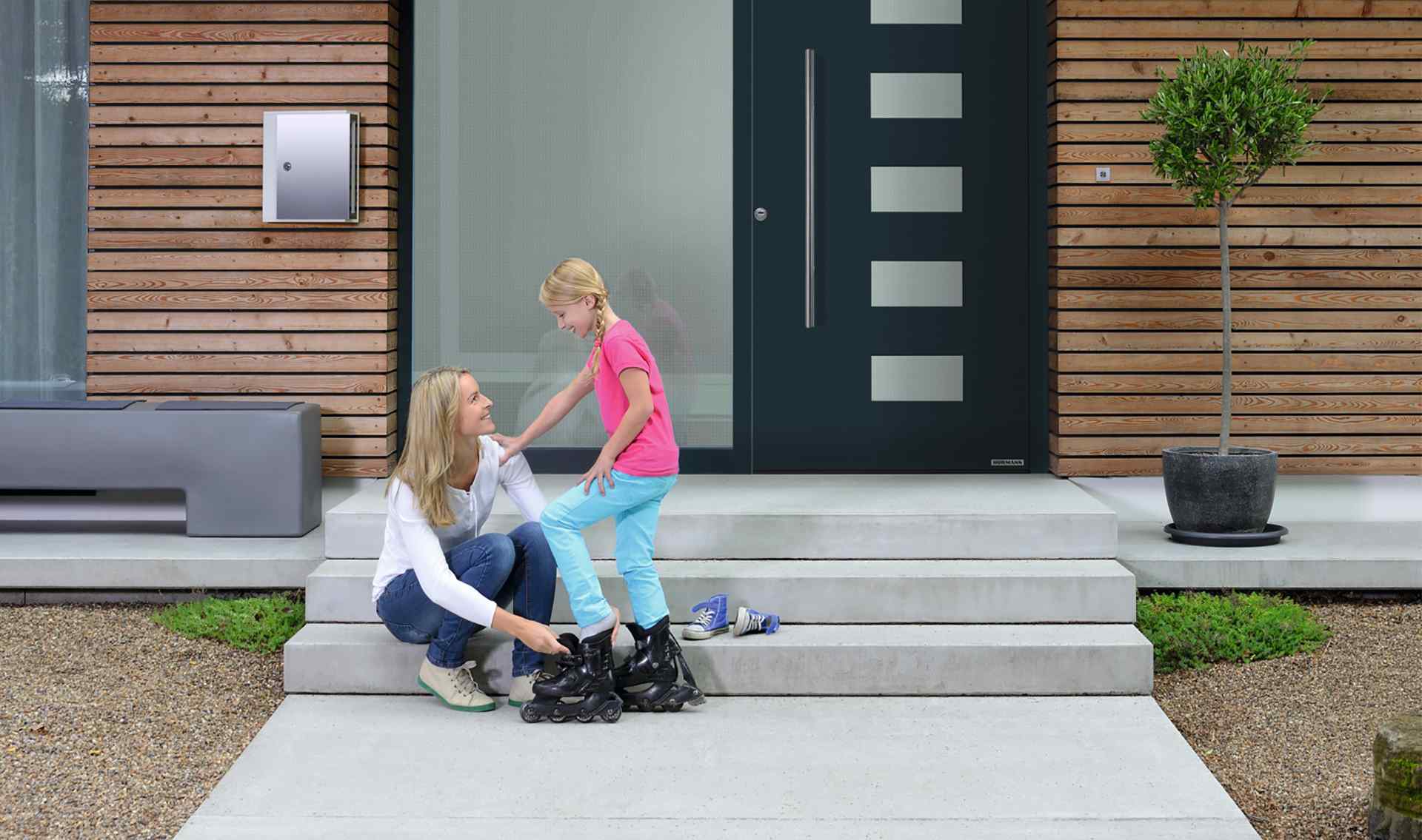 Hörmann Haustür ThermoSafe anthrazit mit Glasfeldern — Mutter und Kind vor modernem Holzfassadenhaus